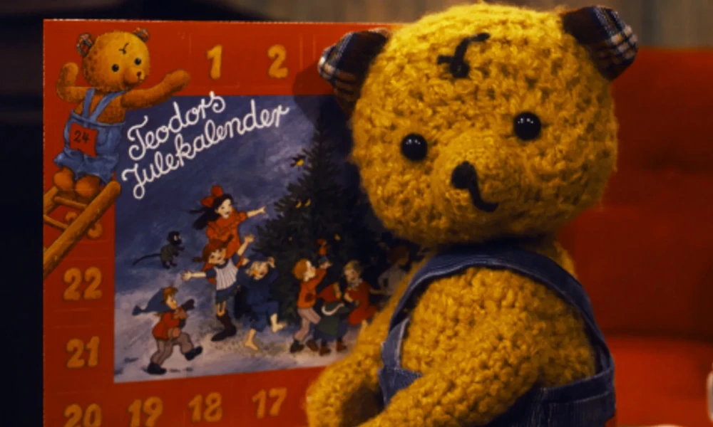 Den gule bamsen Teodor foran en illustrert adventskalender med nummererte luker fra NRK-serien Teodors julekalender.